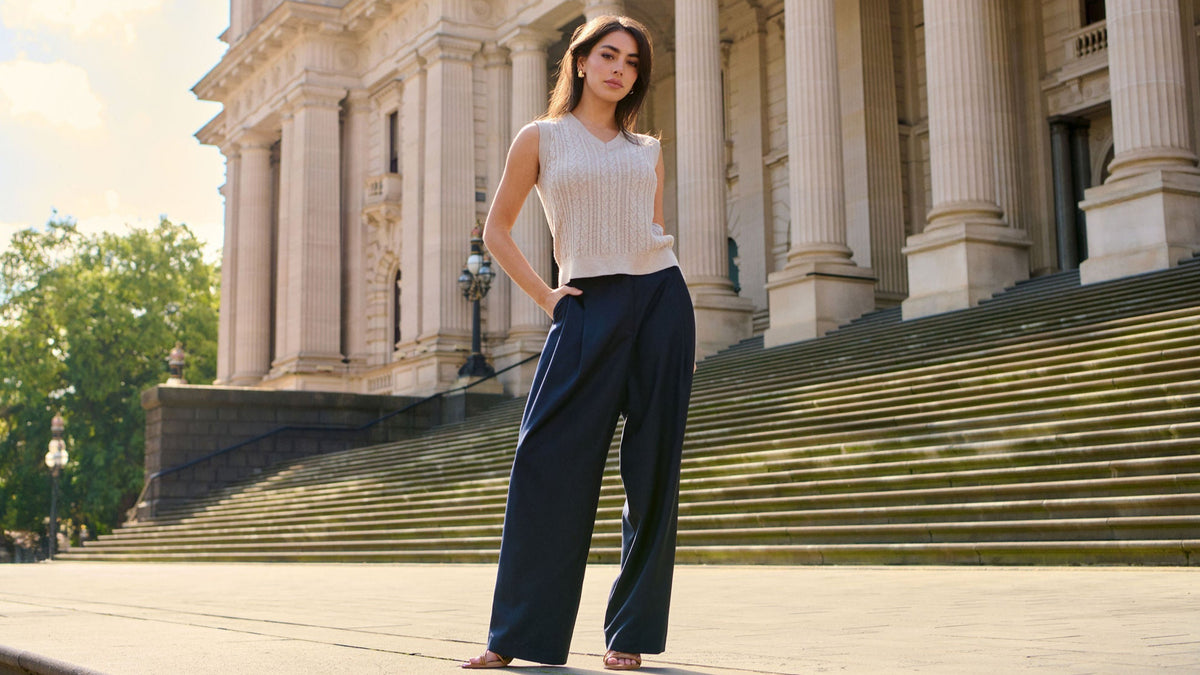 Woman standing in front of a large building with columns wearing meino wool wide leg pants and a cable knit vest made with the correct proportions and fit for petite women
