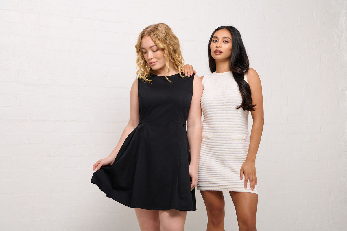 Two women wearing black and white petite sleeveless dresses that fits their form against a plain background. One is wearing a petite LBD (little balck dress) and the other is wearing a petite Chanel style white sleeveless dress. Both dresses made to perfectly fit the proportions of shroter women.